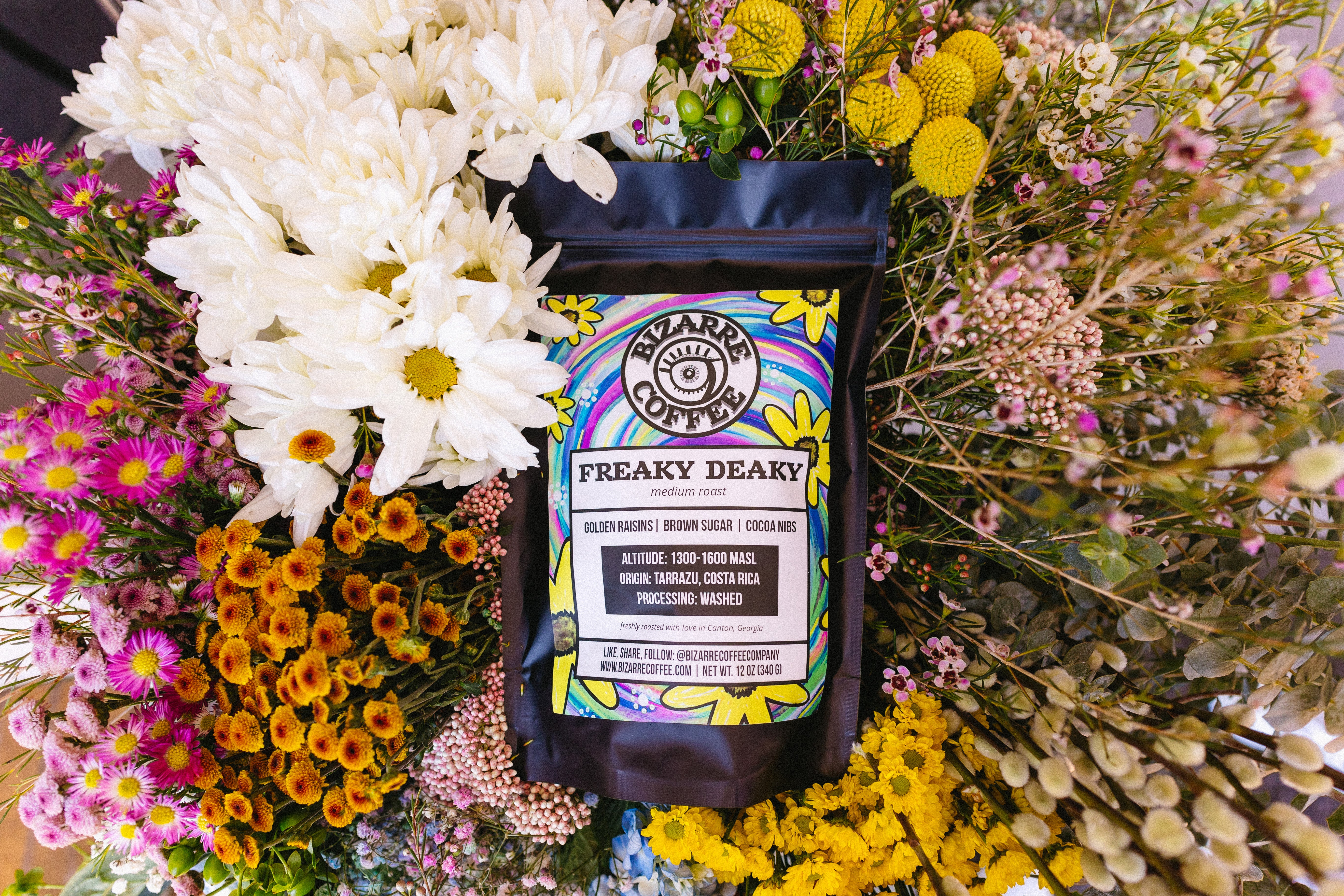 A bag of Freaky Deaky Bizarre Coffee with flowers behind it.