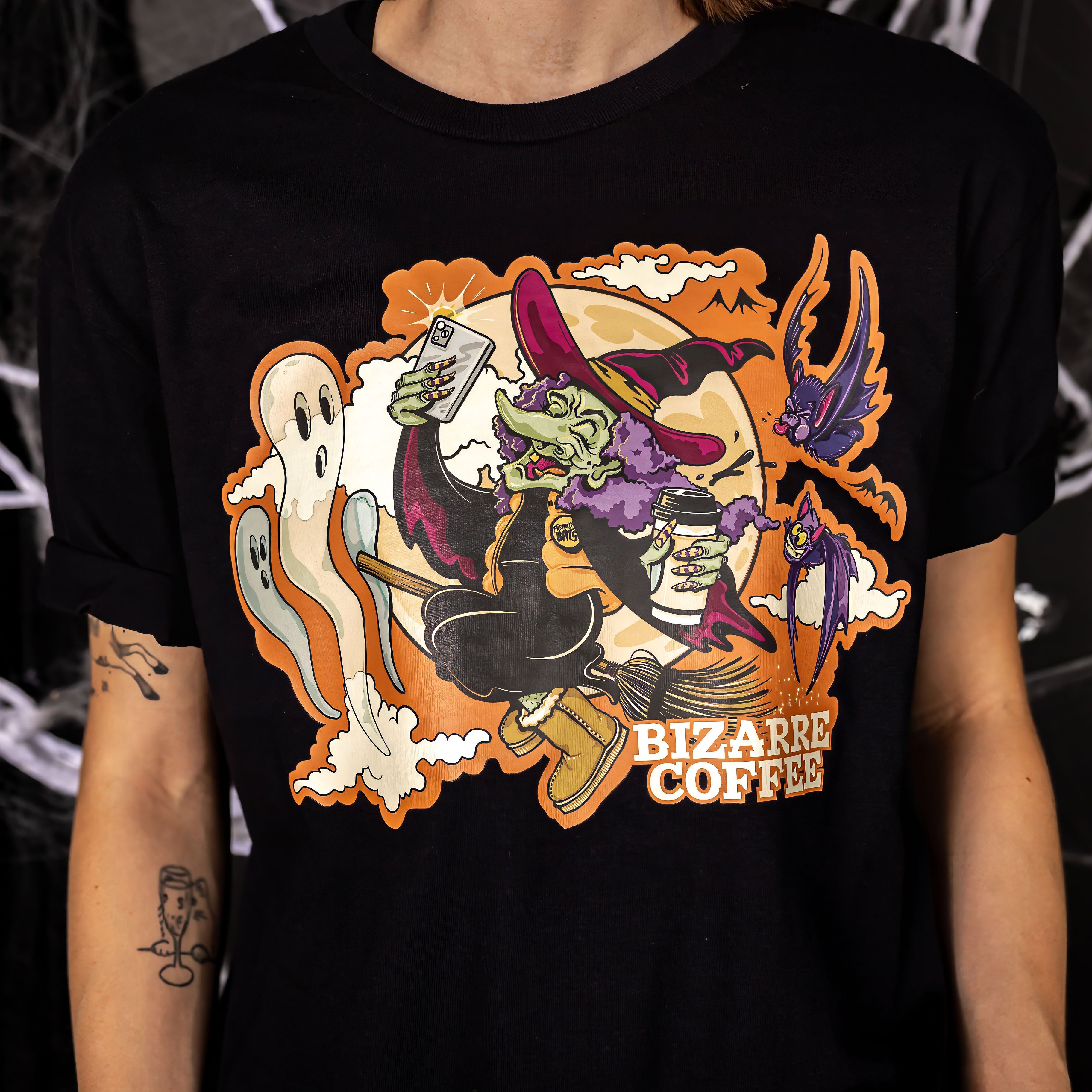 A t-shirt with a custom design featuring a witch on a broom holding a coffee cup.