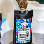 A scoop pouring Bizarre Coffee's Earthling roast coffee beans into a bag on top of a scale. 