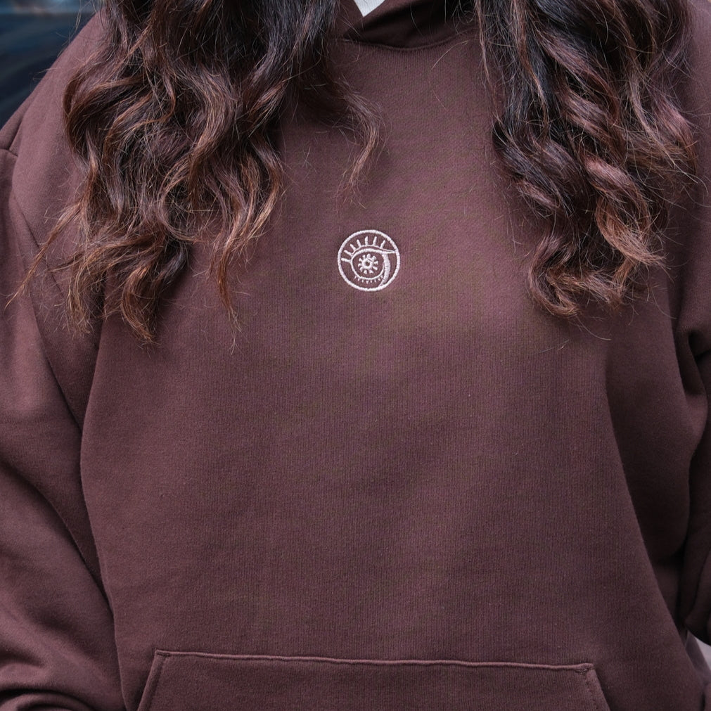 Brown hoodie with a logo worn by a person, on a blurred background