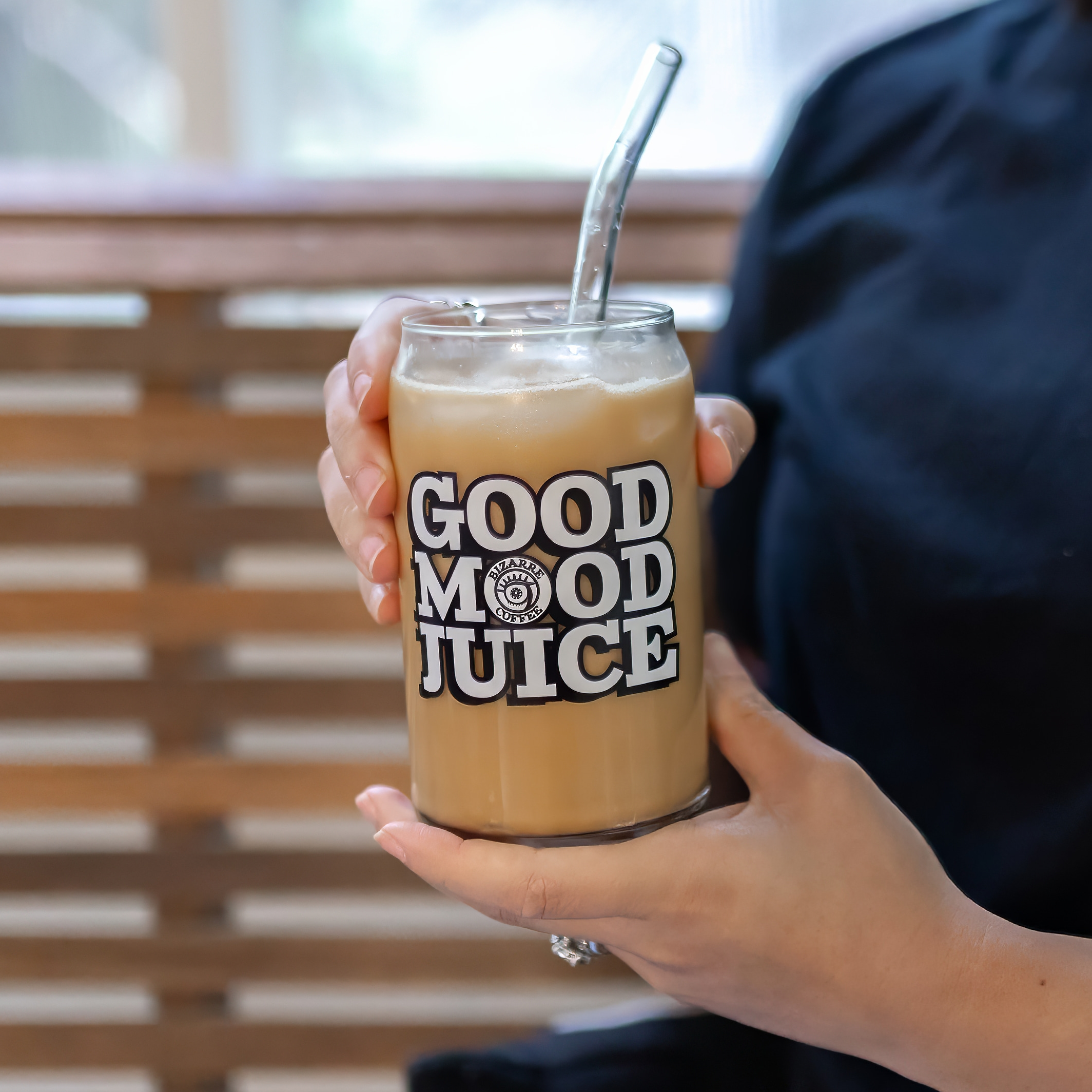 A glass beer cup that says Good Mood Juice, has iced coffee inside and a glass straw.
