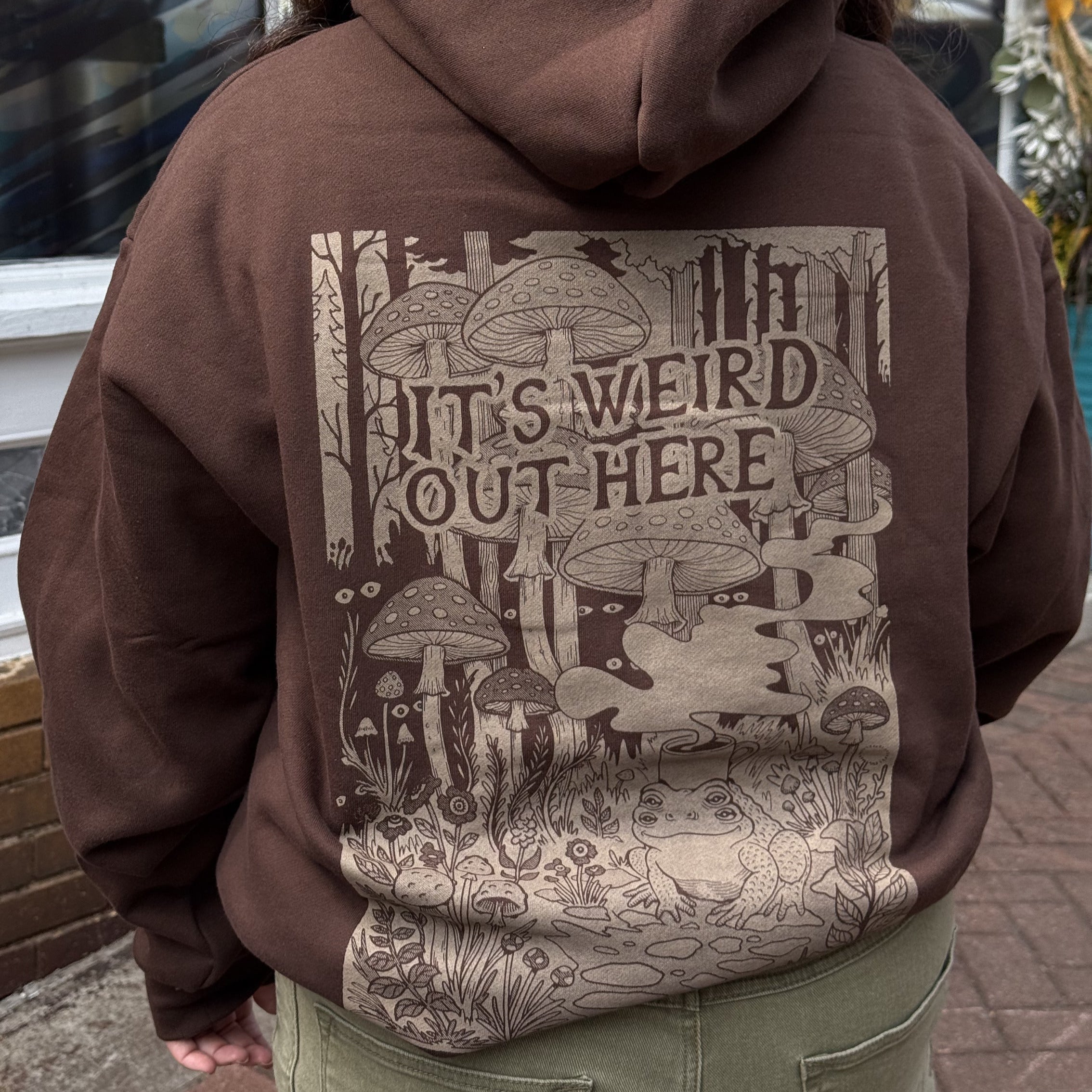 Person wearing a brown hoodie with a graphic design and text on the back.