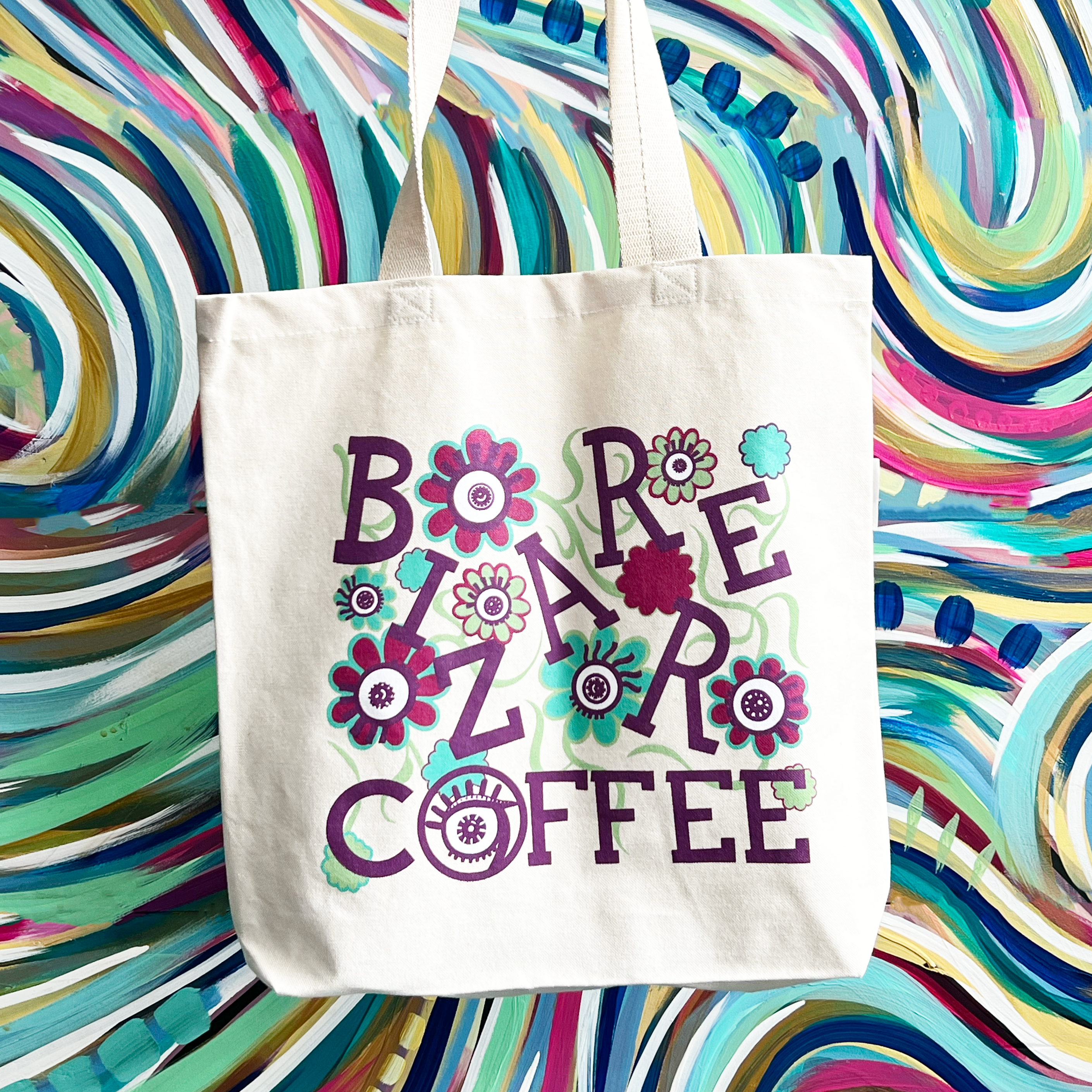 A canvas tote bag that says Bizarre Coffee in purple letters with flowers and eyes.