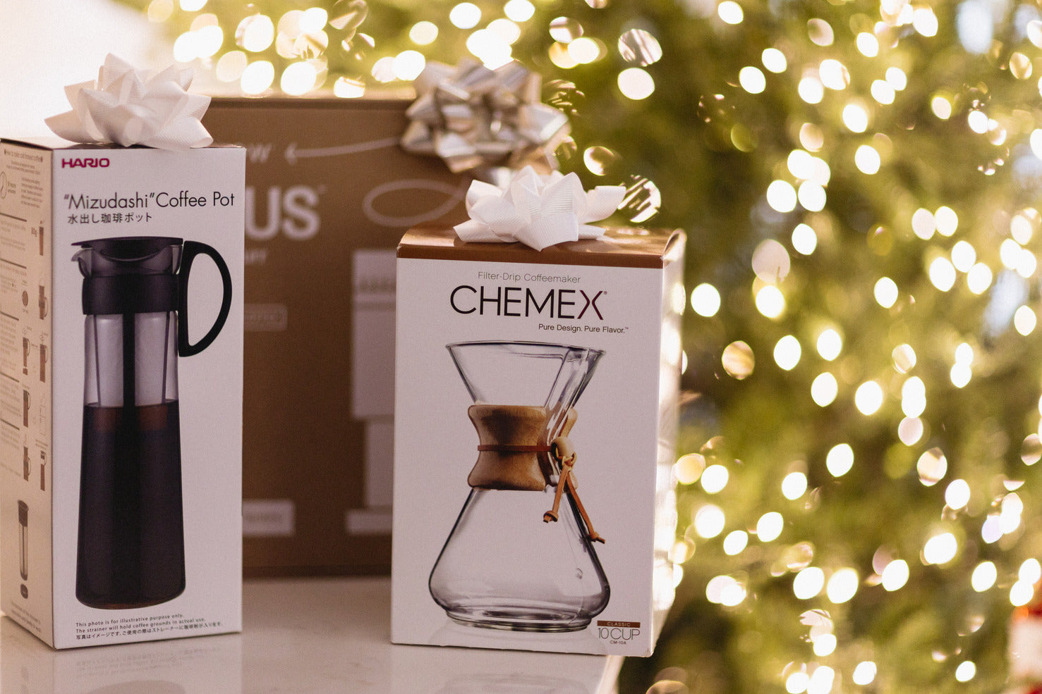 Coffee Gear in box sitting on a table in front of a Christmas Tree with Lights.
