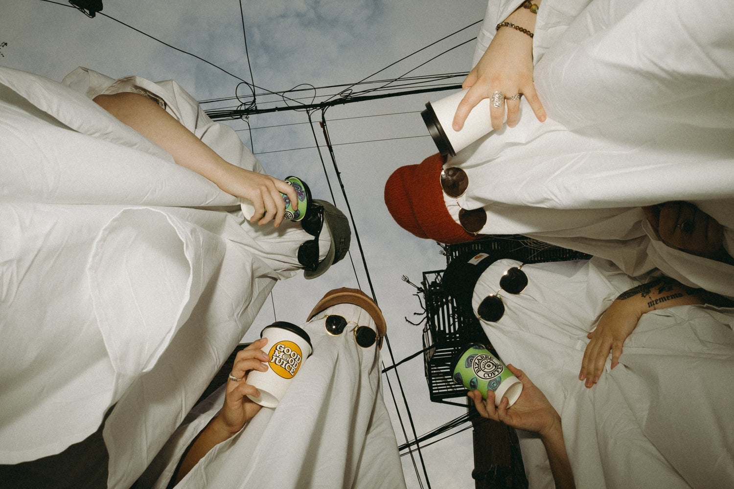 A picture of people wearing ghost costumes looking down towards the camera while holding lattes.