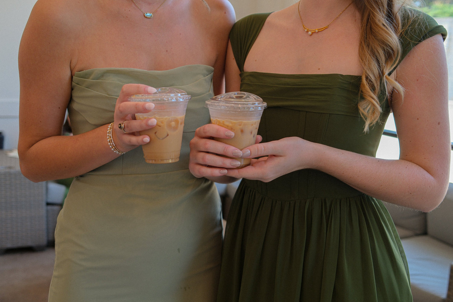 Two women in formal dresses while holding on to iced coffees.