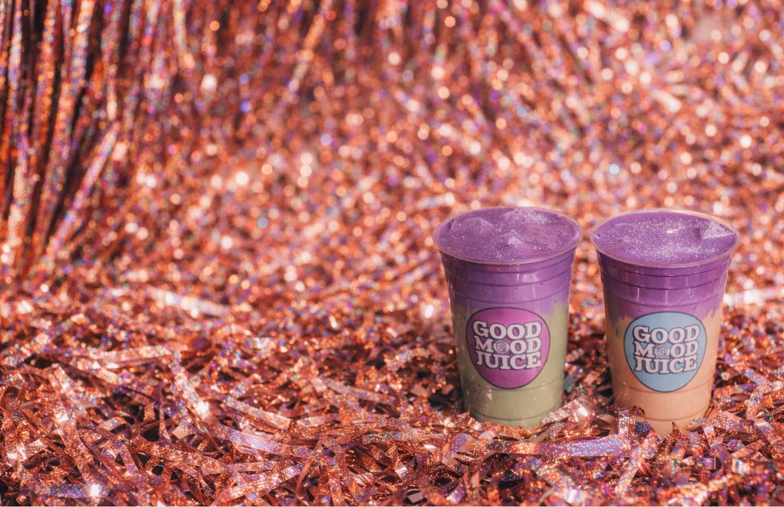 Two purple cups with 'Good Mood Juice' label on a glittery pink background
