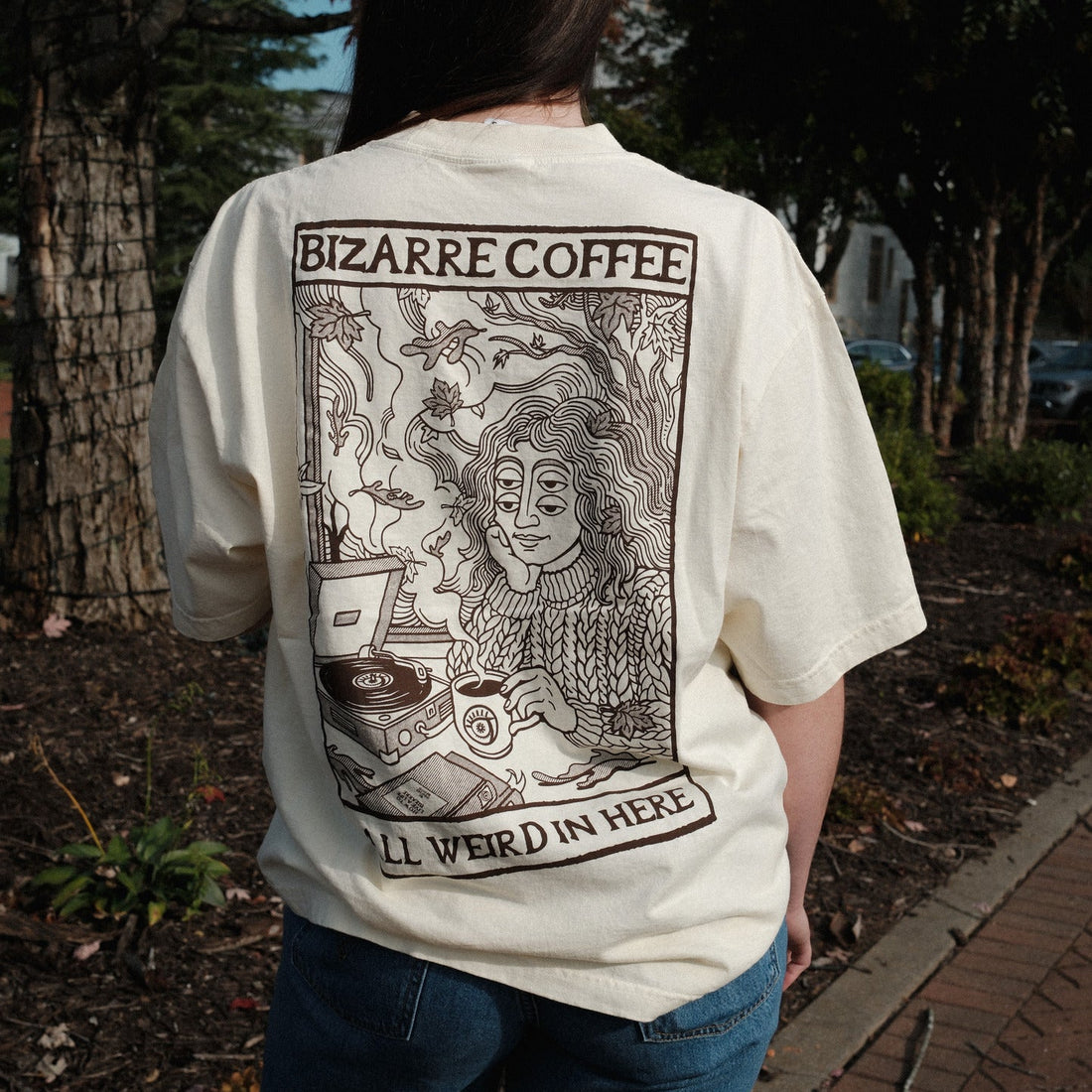 Person wearing a white t-shirt with a graphic design and text, standing outdoors.