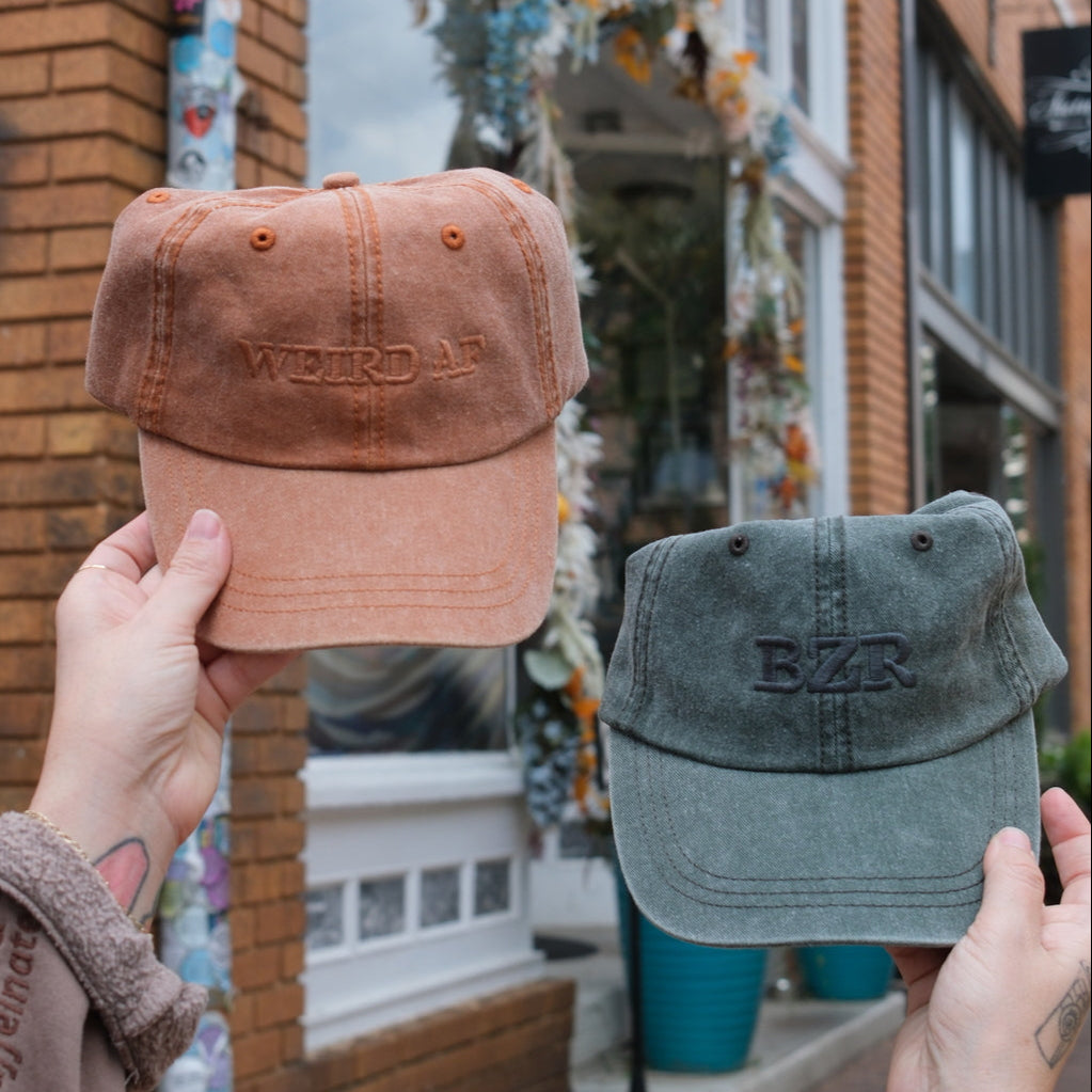 Two hats, one brown and one green, held up in front of a coffee shop.