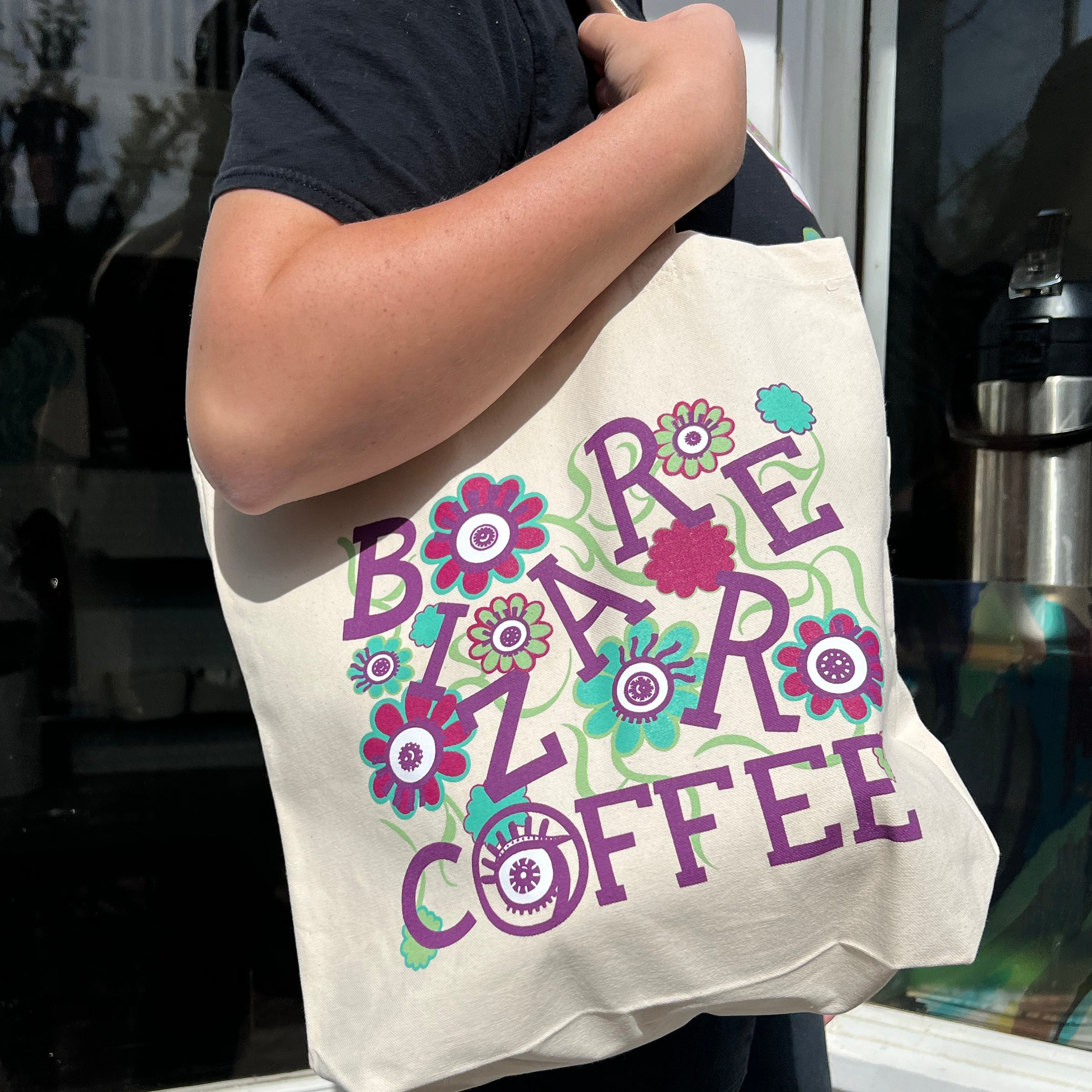 A canvas tote bag that says Bizarre Coffee in purple letters with flowers and eyes.